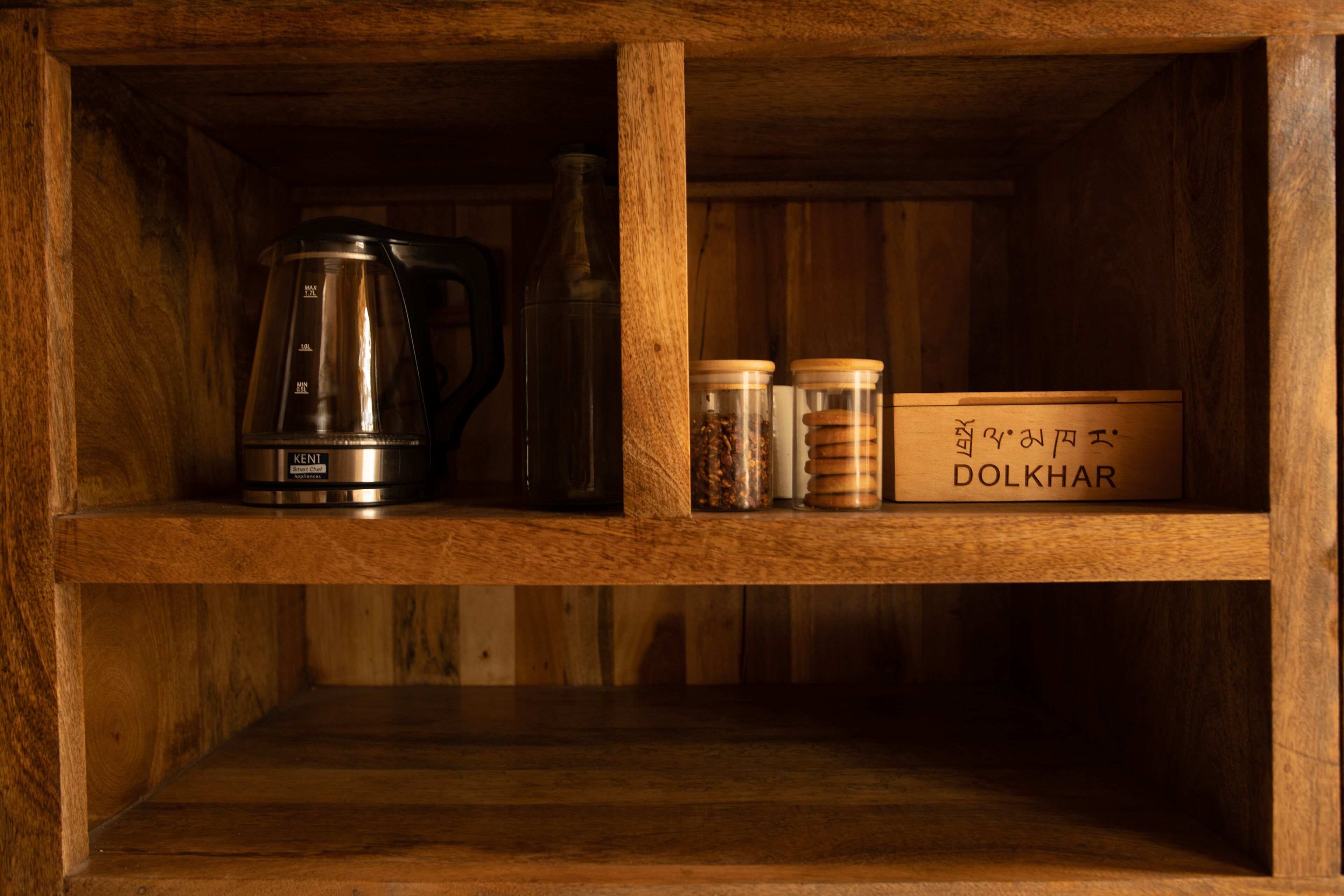 A wooden shelf with a coffee maker, a glass bottle, and jars labeled 'DOLKHAR'.