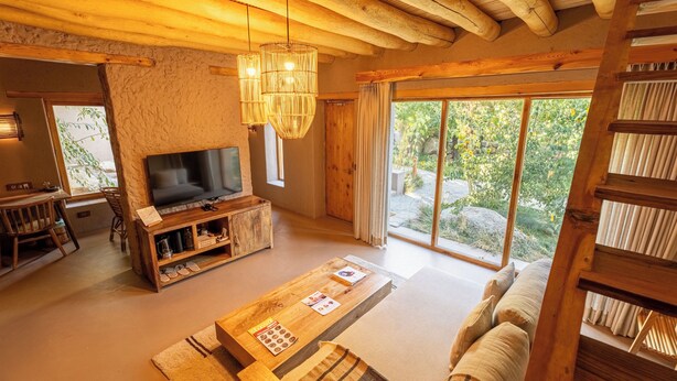 Ein gemütliches Wohnzimmer mit Fernseher, Holzmöbeln und einem großen Fenster mit Blick ins Freie.