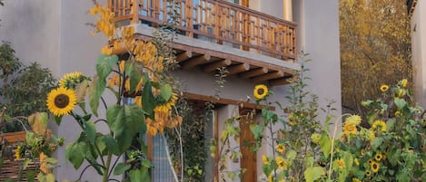 Un edificio de dos pisos con un balcón, rodeado de plantas y flores.