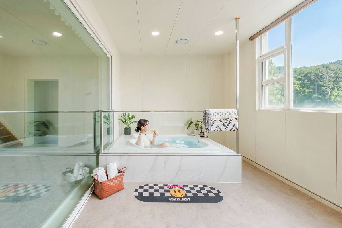 Ein modernes Badezimmer mit einer Duschkabine, einer Badewanne und einem großen Fenster mit Blick auf ein bewaldetes Gebiet.