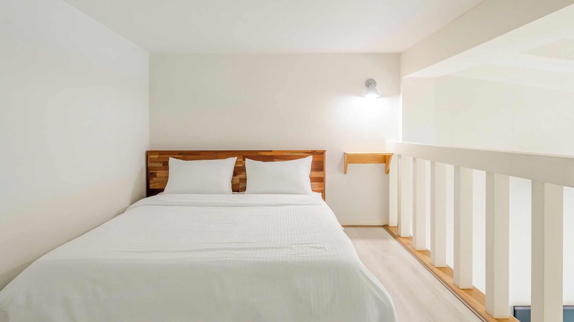 A bedroom with a wooden headboard, a white bedspread, and a nightstand with a wall-mounted lamp.