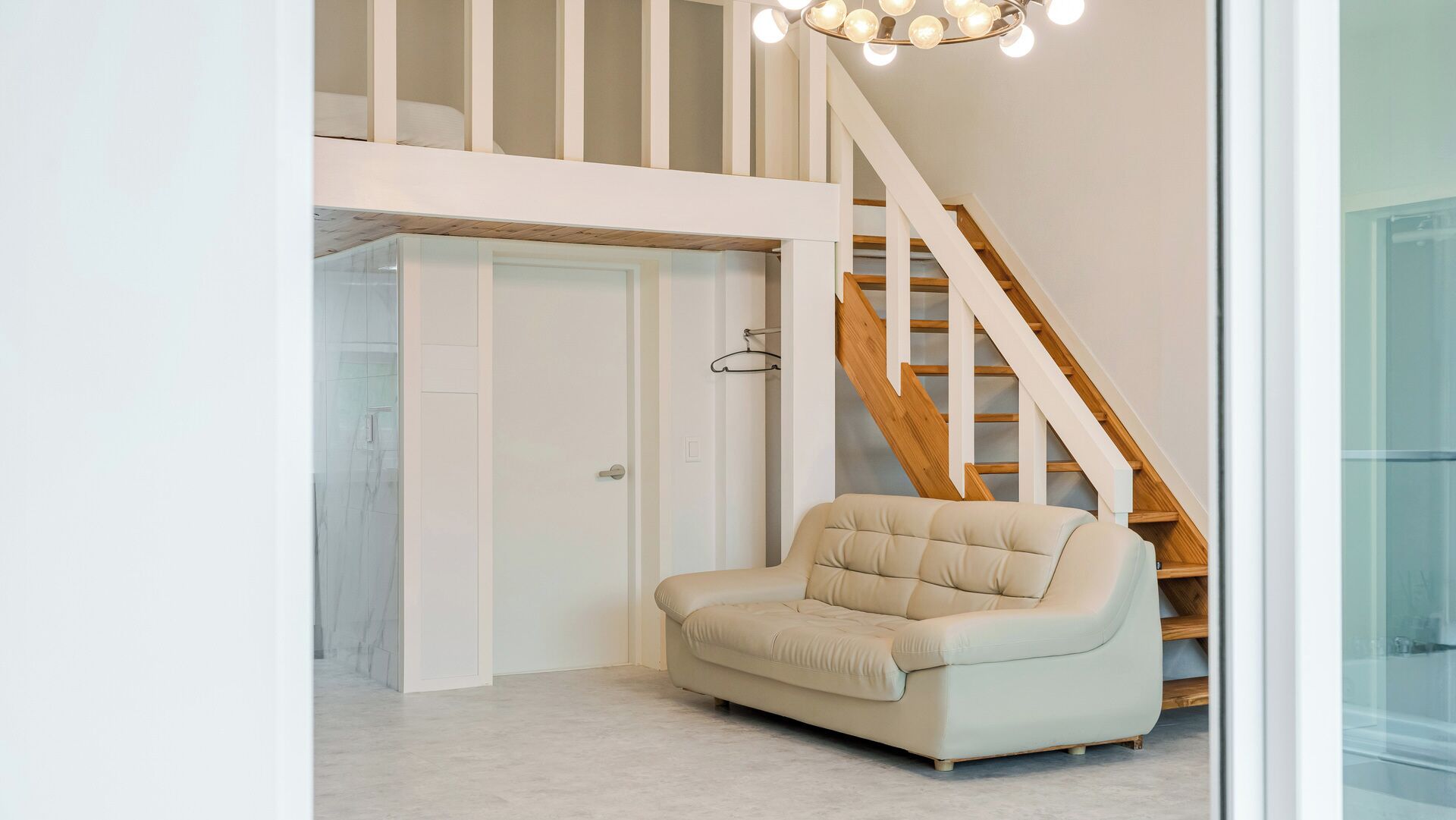 A modern interior with a staircase, a beige armchair, and a glass door leading to a shower area.