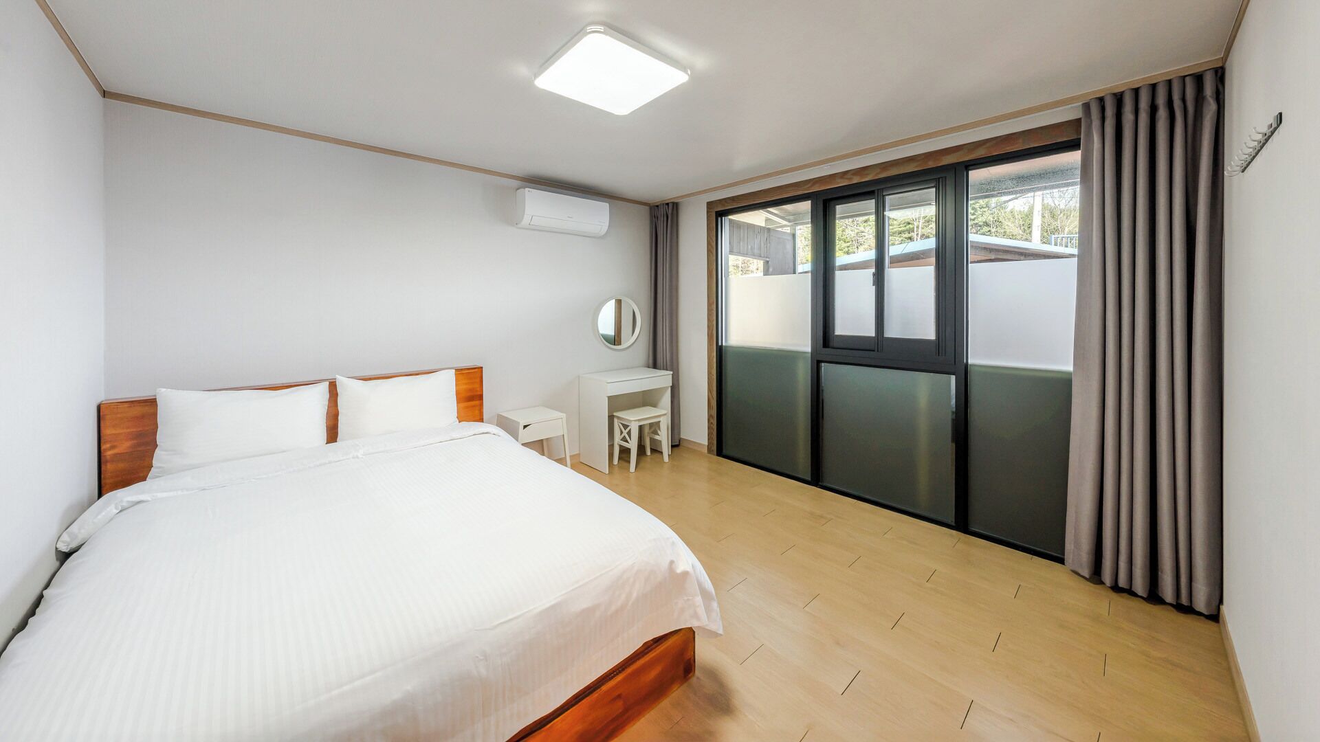 A bedroom with a bed, a desk, a chair, a mirror, and a window with curtains.