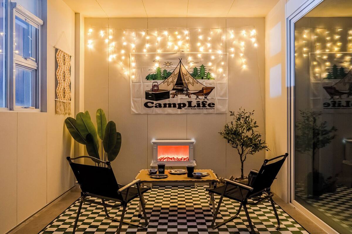 Eine gemütliche Ecke mit kariertem Boden, einem Kamin, zwei Sesseln und einem 'CampLife'-Banner.