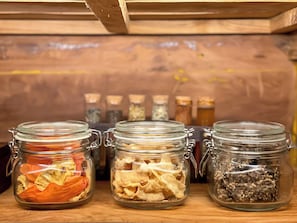 Three glass jars with metal clasps containing dried herbs and spices on a wooden shelf.