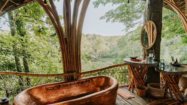 A rustic bathroom with a large clay bathtub, a wooden-framed mirror, and a small table with toiletries. - Bambu Indah Resort (Ubud)