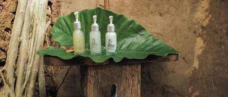 A wooden stand with three bottles of shampoo and conditioner on a green leaf.