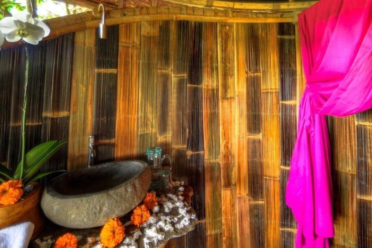 A traditional bamboo room with a stone basin, a hanging shower, and a pink curtain.
