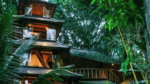 A multi-level wooden structure surrounded by lush greenery, with a thatched-roof entrance and multiple balconies. - Bambu Indah Resort (Ubud)