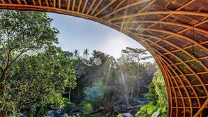 A bamboo structure with a curved roof overlooking a lush garden with various plants and a small water feature. - Bambu Indah Resort (Ubud)