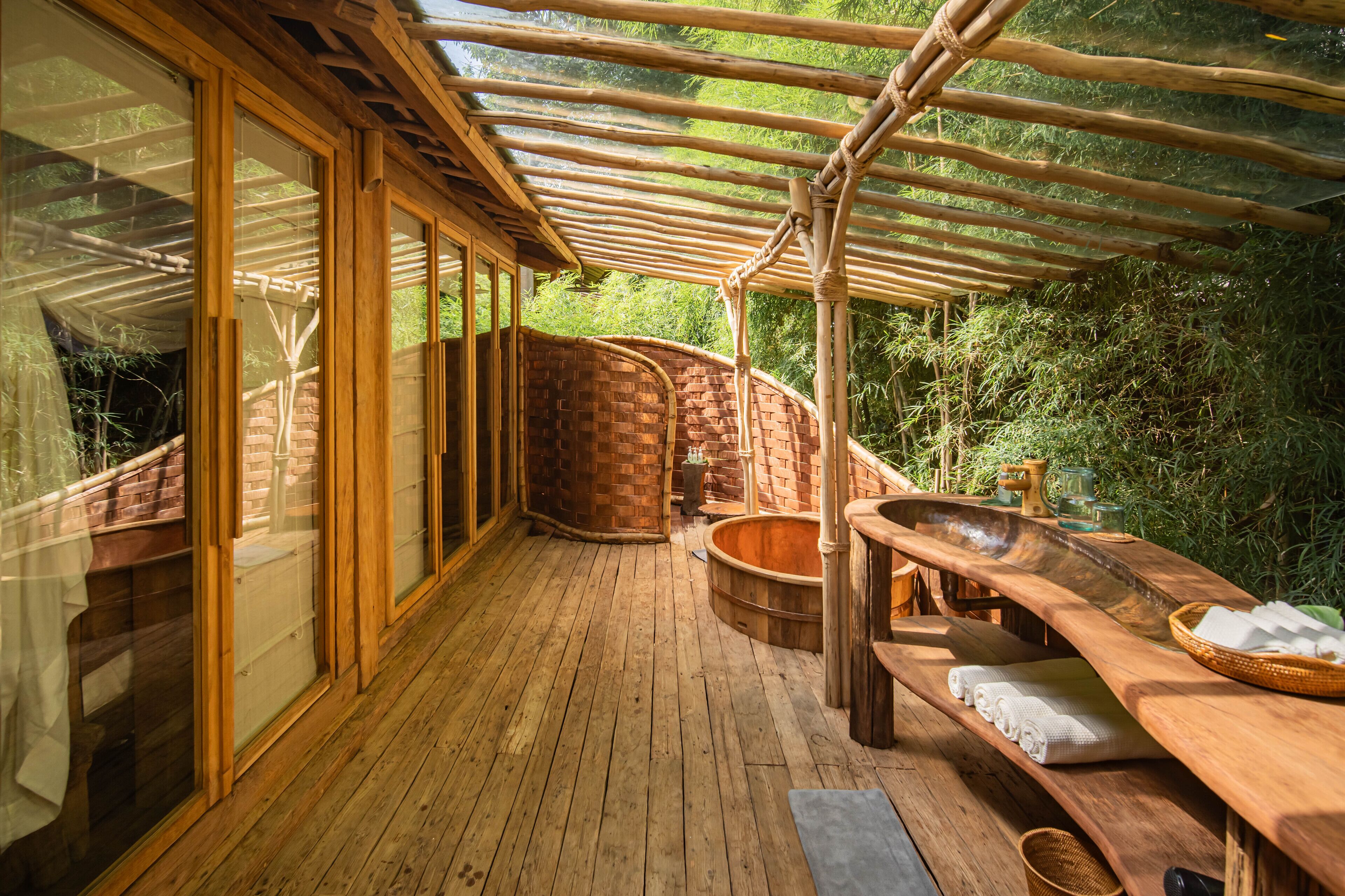 A wooden deck with a glass enclosure, a brick wall, and a wooden bench with towels.