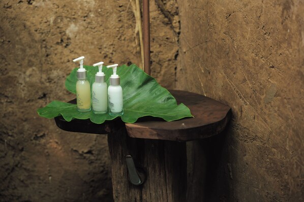 A wooden stool with a green leaf and three bottles of liquid with pumps on top. - Bambu Indah Resort (Ubud)