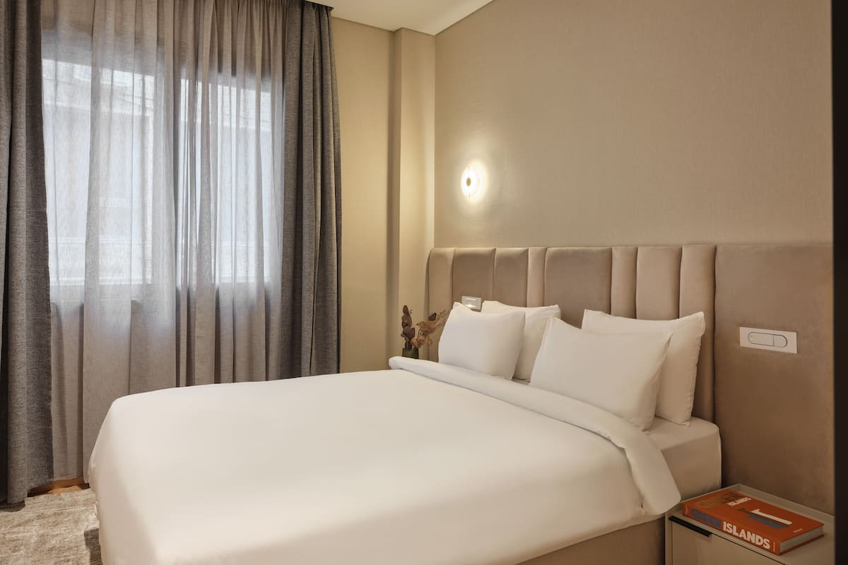 A hotel room with a large bed, a nightstand, a lamp, and a window with curtains.