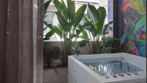 A modern bathroom with a large bathtub, large green plants, and a colorful abstract painting on the wall. - Nur Outline Aparthotel (Athens)