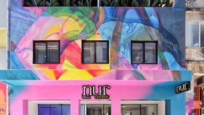 A colorful building with a vibrant mural, a storefront with a sign reading "nurt outline," and a balcony with plants. - Nur Outline Aparthotel (Athens)