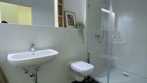 Un baño con lavamanos blanco, inodoro y ducha con mampara de vidrio.