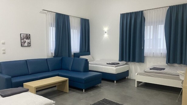 Una sala de estar moderna y luminosa con un sofá azul, una cama blanca y una pequeña mesa.
