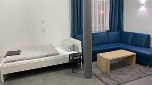 Una habitación pequeña y moderna con una cama blanca, un sofá azul, una mesa de centro de madera y un pilar grande.