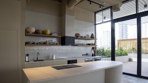 Une cuisine moderne dotée d’un grand îlot central, d’étagères intégrées ornées d’objets décoratifs et offrant une vue sur la ville grâce à de grandes fenêtres.