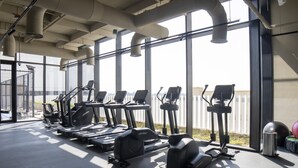 A gym with various exercise equipment, large windows, and a view of the outside. - Modern Executive Studio Burj View Upside Living (Dubai)