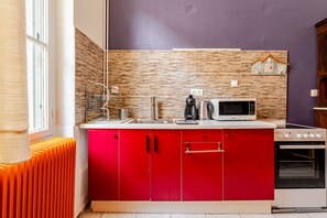 A compact kitchen with a red cabinet, a microwave, a kettle, and a stove.