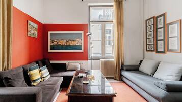 A living room with a red accent wall, a large window with curtains, a sofa, a coffee table, and framed artwork on the wall.