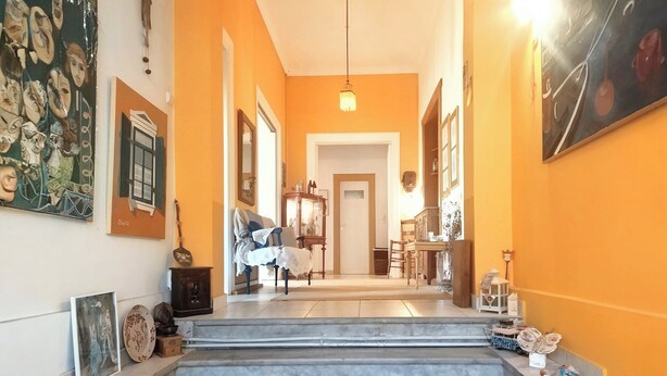 Un couloir avec un escalier menant à une salle à manger, des œuvres d’art encadrées accrochées aux murs et un luminaire suspendu.
