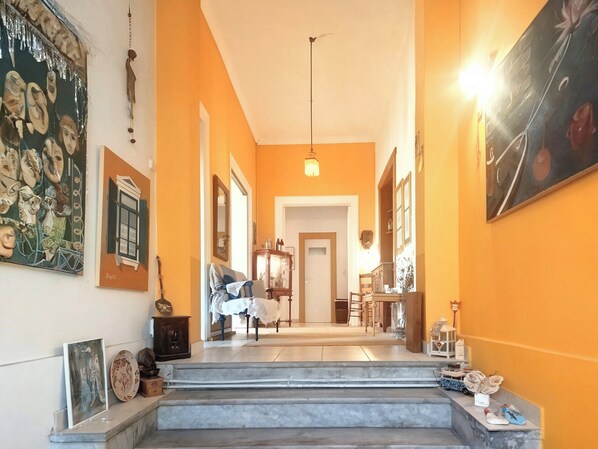 A hallway with a staircase leading to a dining area, framed artwork on the walls, and a hanging light fixture. - Acropolis Masterpiece Neoclassical Mansion (Athina)