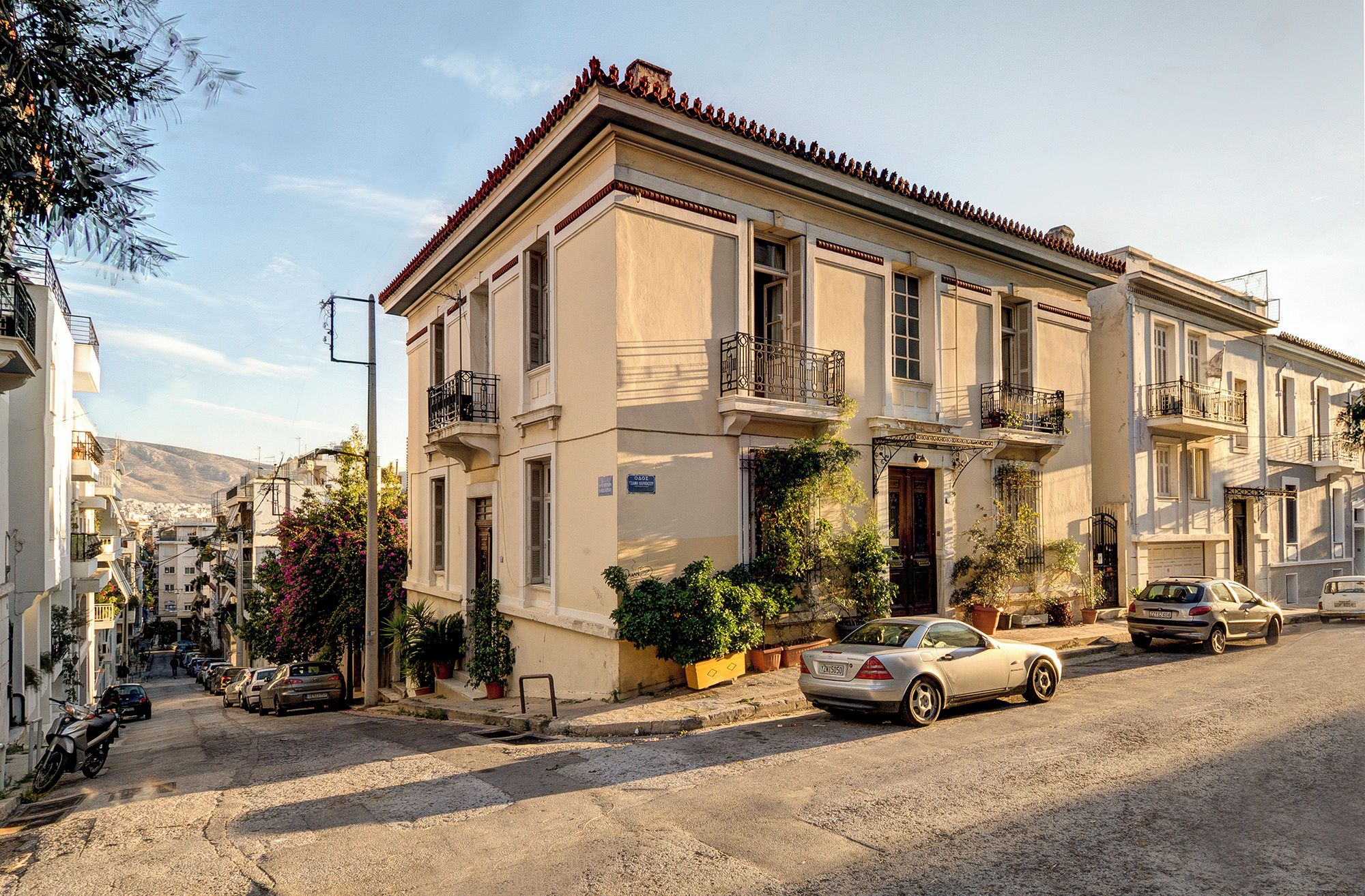 A two-story building with a balcony, parked cars, and potted plants.