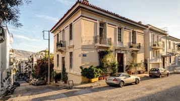 A two-story building with a balcony, parked cars, and potted plants.