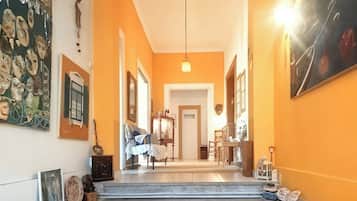 A hallway with a staircase leading to a dining area, framed artwork on the walls, and a hanging light fixture.