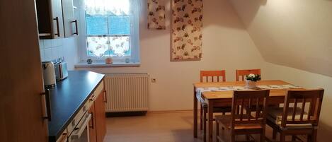 A compact kitchen with a dining area, featuring a radiator, a window with curtains, and a table with chairs.
