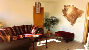 Ein Wohnzimmer mit einer Couch, einem Couchtisch, einer Topfpflanze und einem aufgehängten Tierfell.