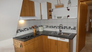 Eine kompakte Küche mit Holdekor-Schränken, einer schwarzen Arbeitsplatte, einer Spüle und einer Rückwand mit Mosaikfliesen.