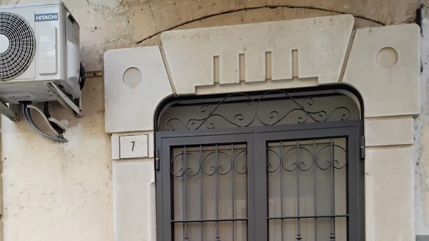 A building entrance with a metal gate, a wall-mounted air conditioning unit, and a vehicle parked nearby. - Casa Manzoni, renovated apartment within walking distance of the sea in Bisceglie.   (Bisceglie)