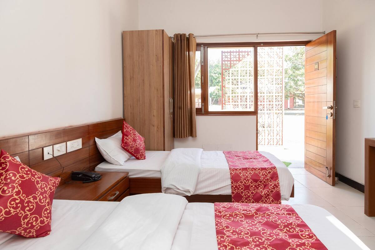 Quarto de hotel com duas camas, um guarda-roupa, mesa de cabeceira com telefone e janela com vista para o exterior.