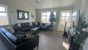 Een ruime woonkamer met een hoekbank, een glazen salontafel en een groot raam met uitzicht op de omgeving.
