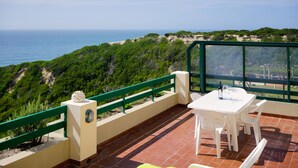 A terrace with a table and chairs, overlooking a coastal landscape with greenery and the sea. - Experience Portugal at its finest: Beach, activities,culture -the perfect blend! (Pataias)