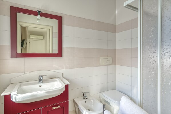 Un baño con lavamanos blanco, tocador rojo y retrete blanco.
