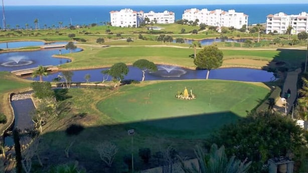 A golf course with multiple ponds and a large open green area, surrounded by white buildings with red roofs.