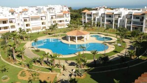 A resort with a central swimming pool, palm trees, and a view of the ocean.