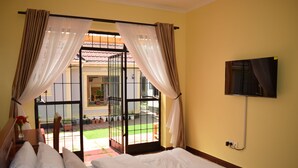 Una habitació d'hotel amb llit, cortines, televisió penjada a la paret i vista al balcó exterior.