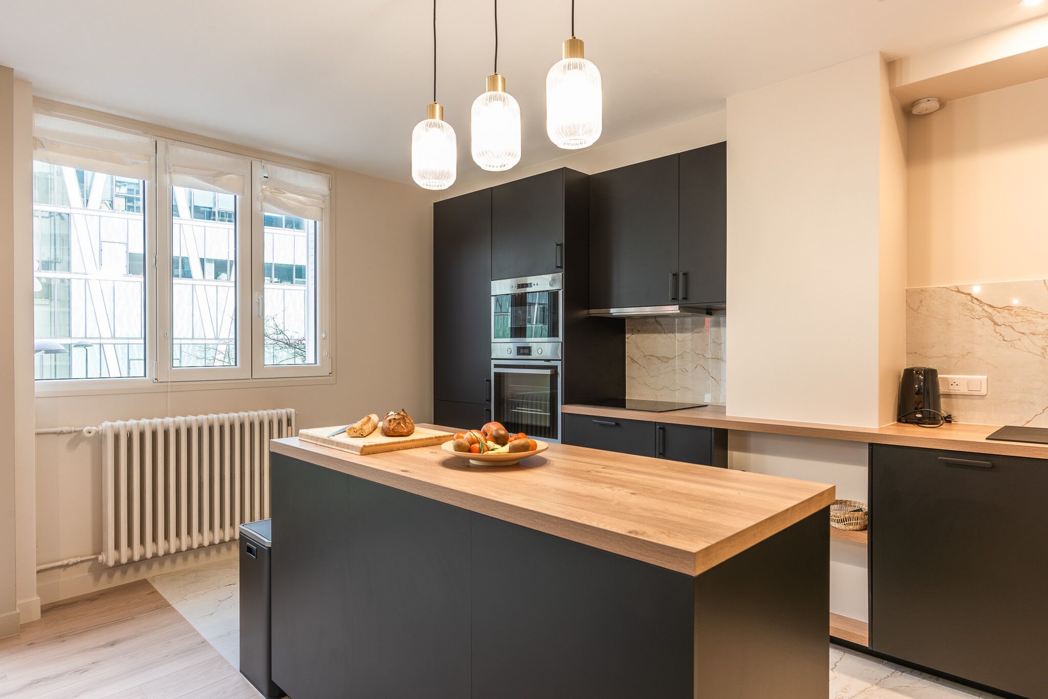 Una cocina moderna con una isla central, armarios negros y un radiador blanco.