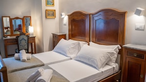 Ein Doppelbett mit zwei Kissen und einem Holz-Kopfstück, ein Nachttisch mit Lampe, ein Schreibtisch mit Stuhl und ein Spiegel.