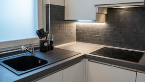 Eine moderne Küche mit einem schwarzen Spülbecken, weißen Schränken und einer schwarzen, gefliesten Rückwand.