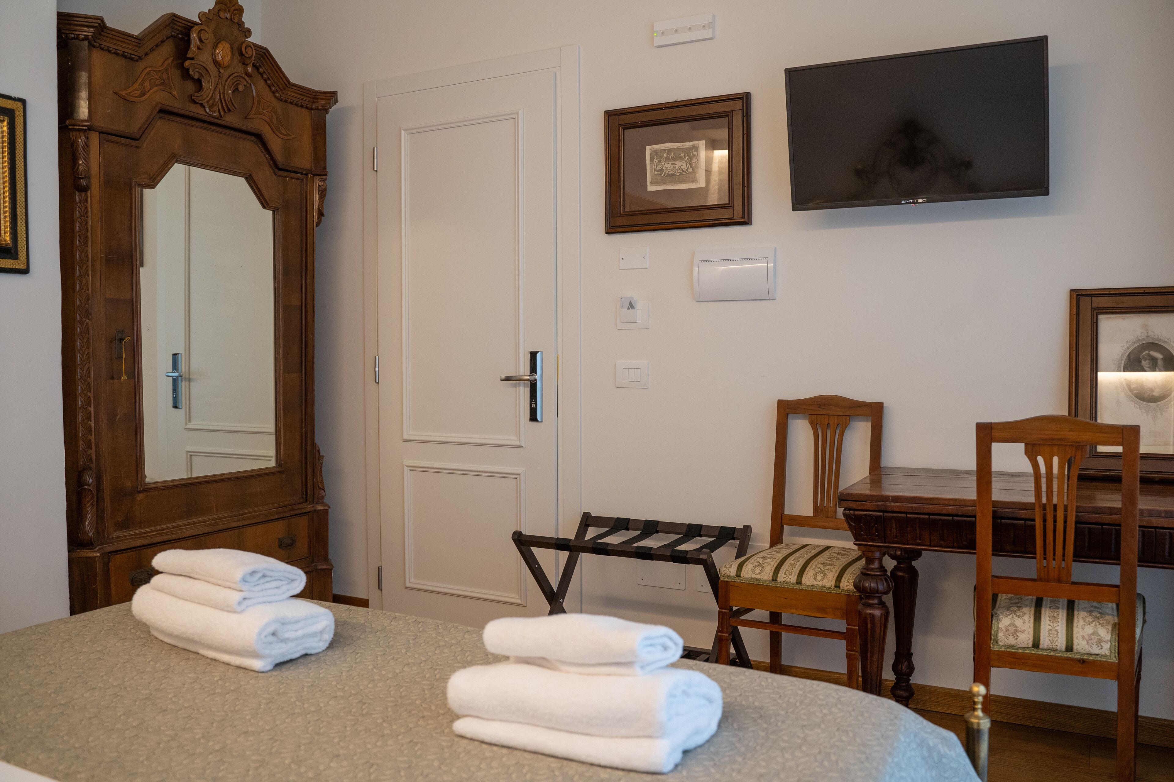 A hotel room with a bed, a wooden dresser, a mirror, a television, and a desk with chairs.