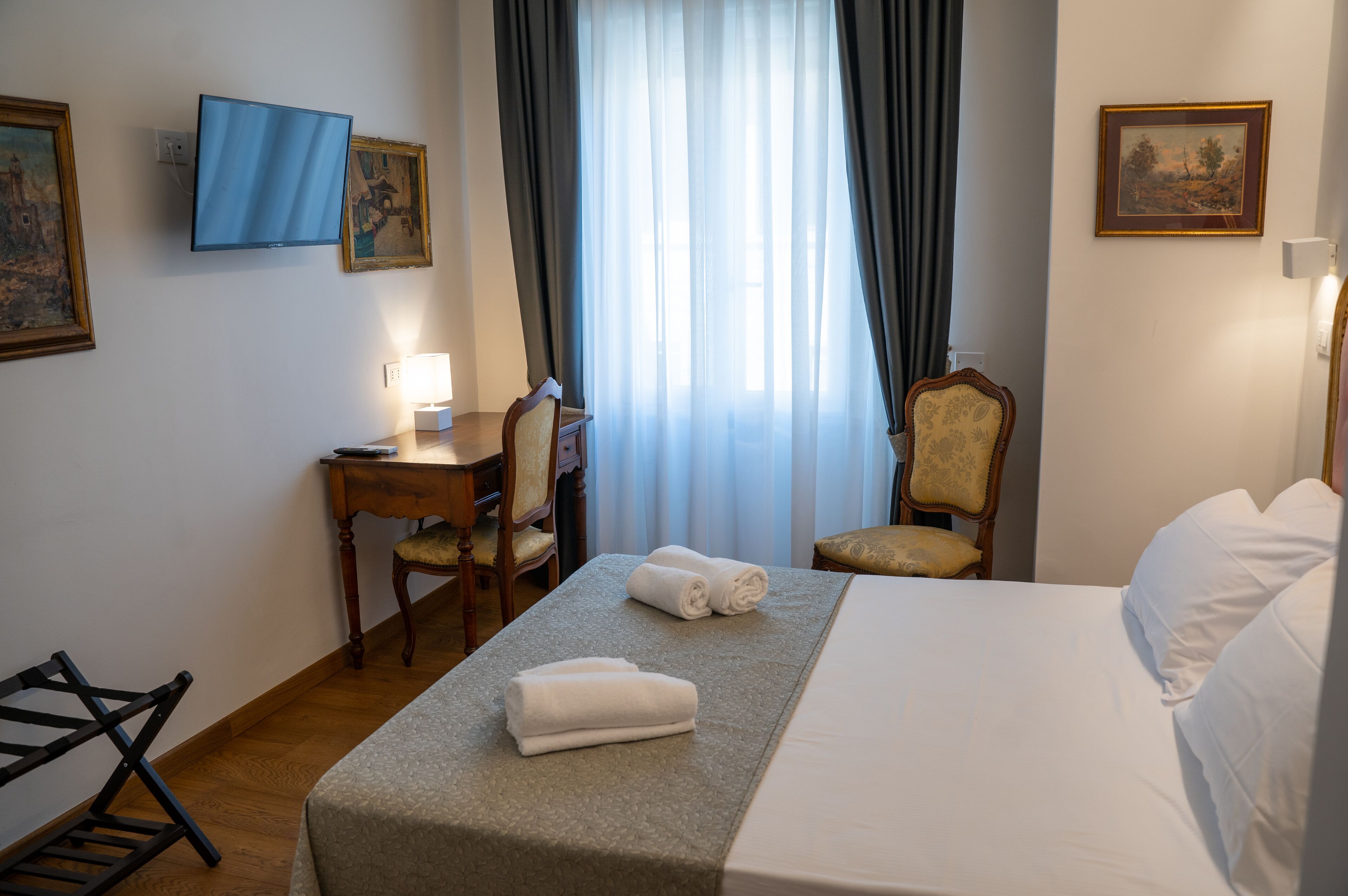 A hotel room with a bed, a desk, a chair, and a television.