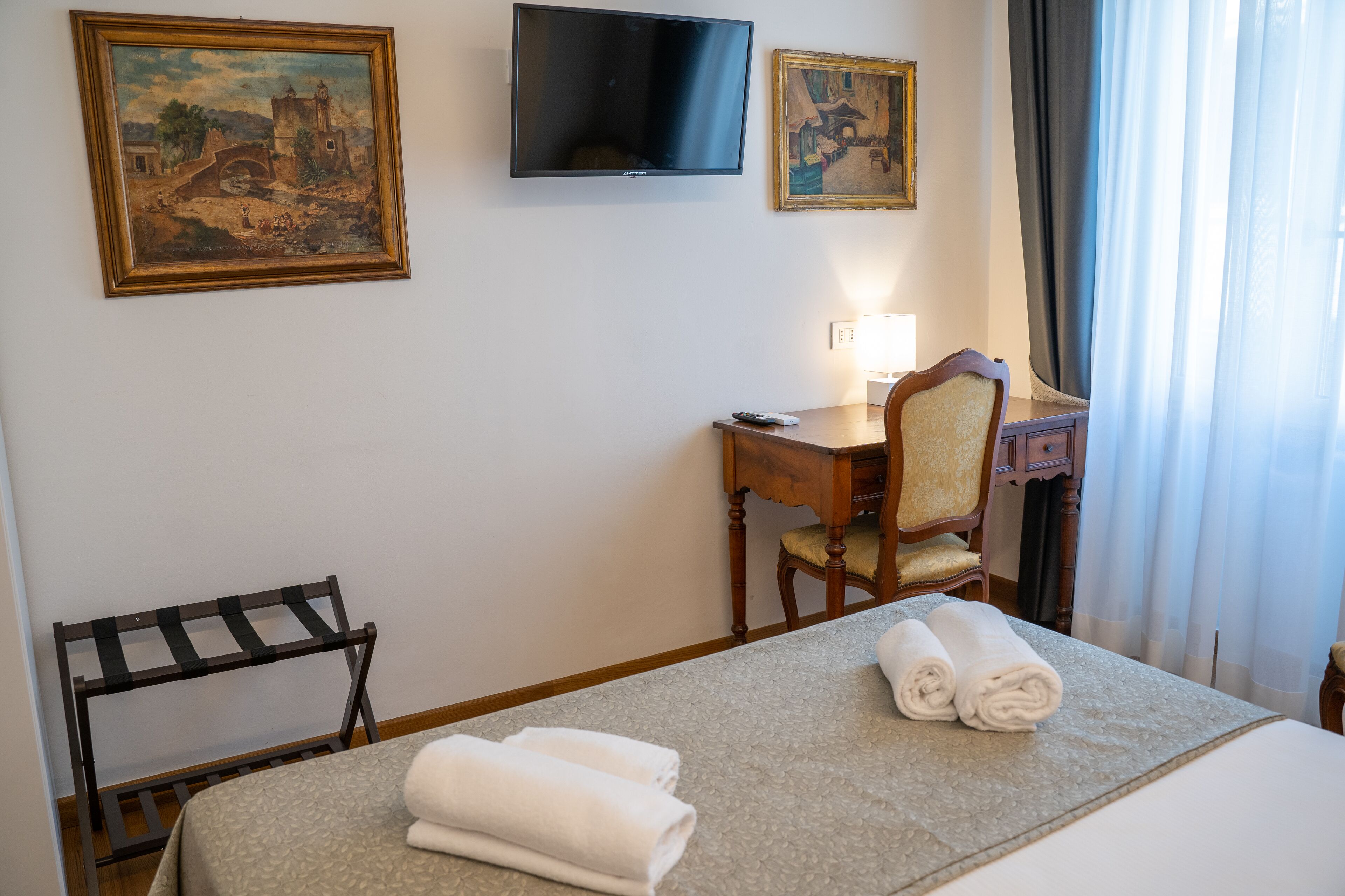 Een hotelkamer met een bed, een bureau, een stoel, een televisie en twee schilderijen aan de muur.