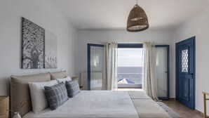 Un dormitorio con una cama grande, vistas al mar a través de una puerta abierta y una lámpara de techo de mimbre.