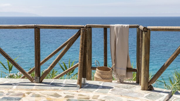 Una terraza de madera con vistas al mar, una cesta tejida y un paño color beige.